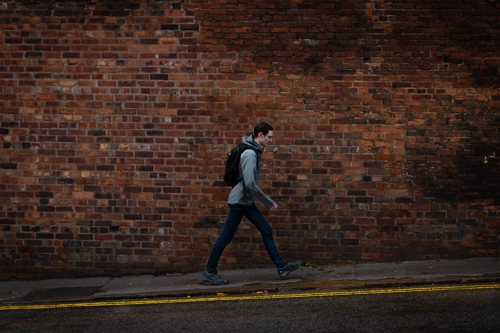 Man walking along the street with brick wall behing them